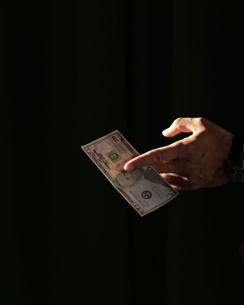 pexels-photo-5921122-5921122 A close-up of a hand holding a US dollar bill against a dark background, highlighting financial themes.